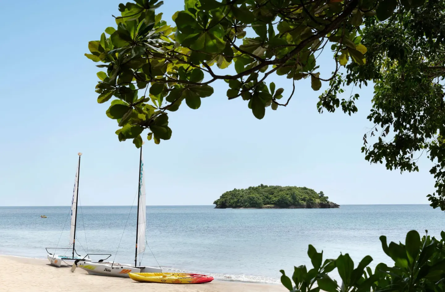 Sandy beach with sailboats, kayaks, and a small island offshore at Sandals Halcyon.