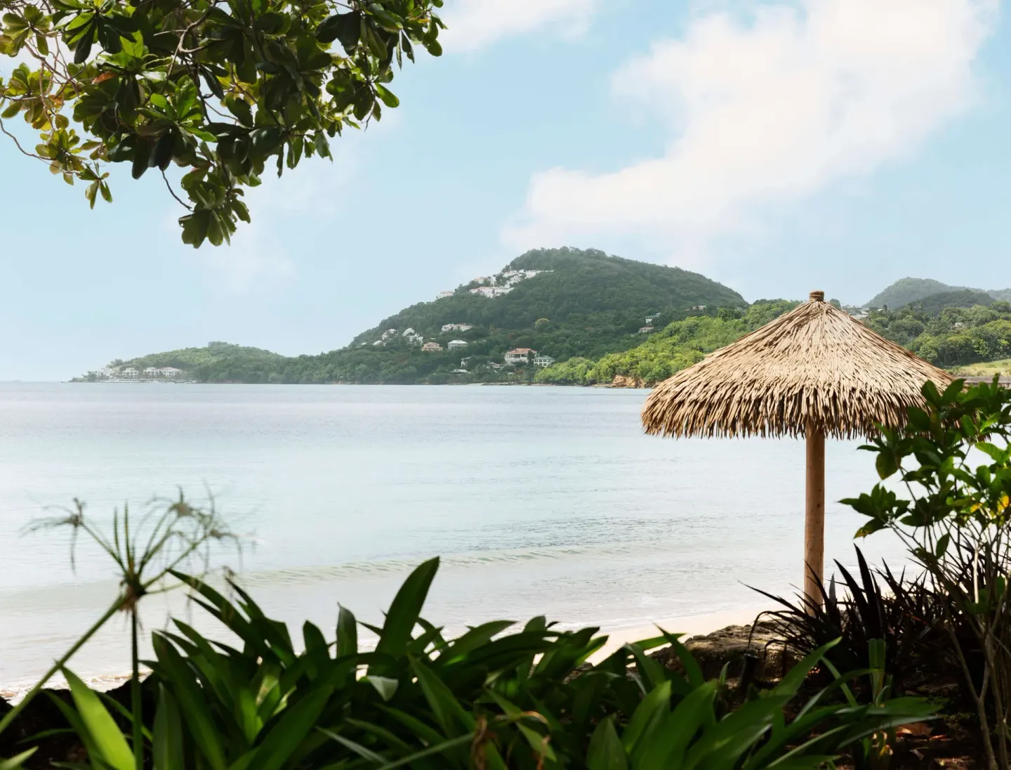 Calm bay, thatched beach umbrella, and green hillside at Sandals Halcyon.