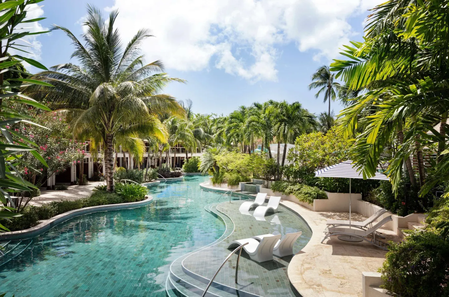 Lagoon-style pool winding between palms, loungers, and guest buildings at Sandals Halcyon.