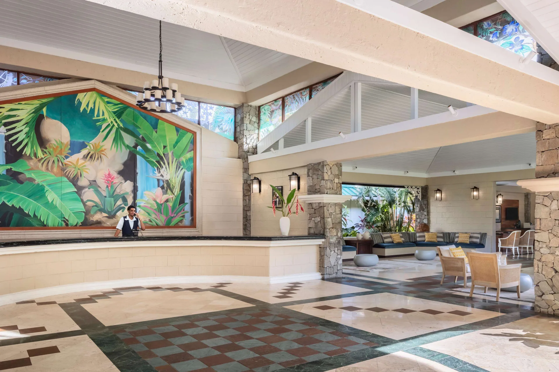 Open lobby with reception desk, tropical mural, and lounge seating at Sandals Halcyon.