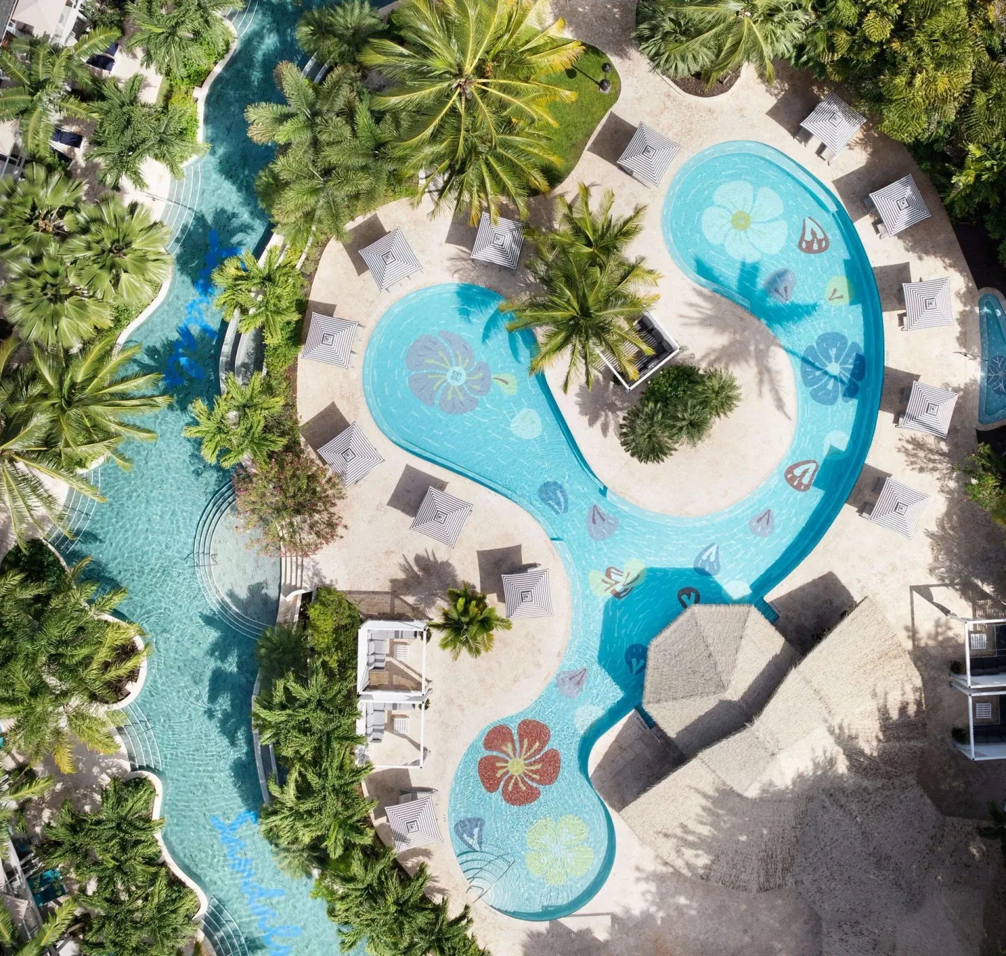 Top-down view of a flower-patterned pool, striped umbrellas, and palms at Sandals Halcyon.