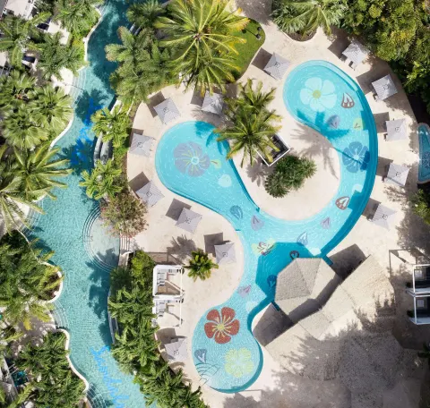 Top-down view of a flower-patterned pool, striped umbrellas, and palms at Sandals Halcyon.