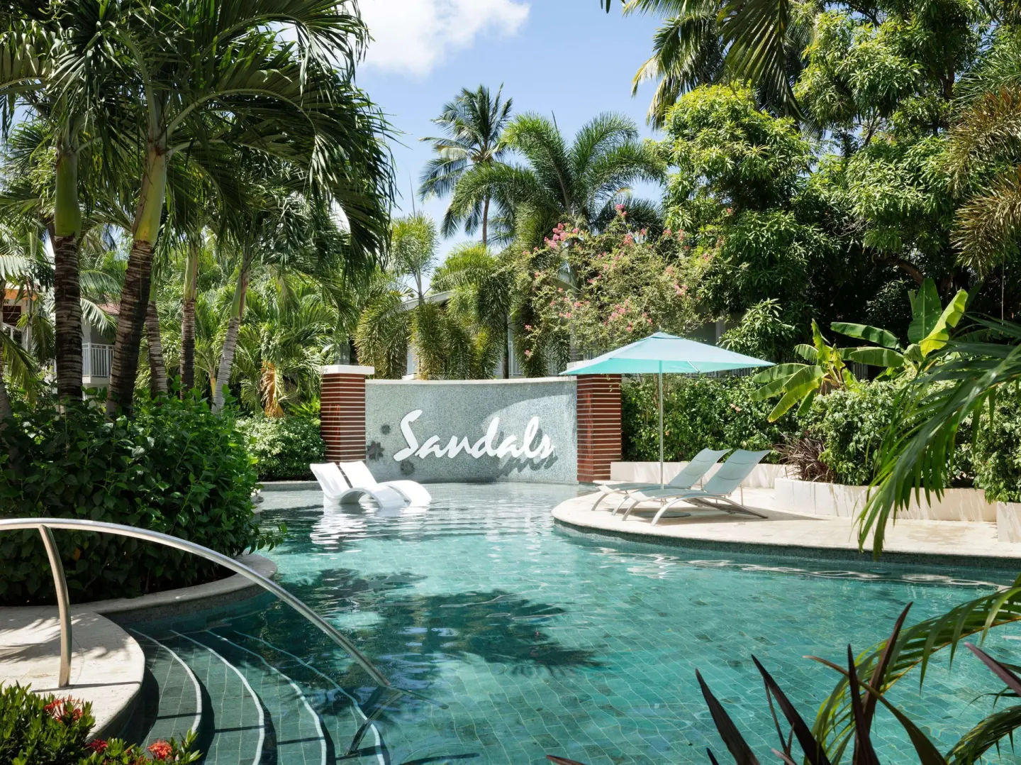 Tropical pool with in-water loungers and a Sandals wall sign at Sandals Halcyon.