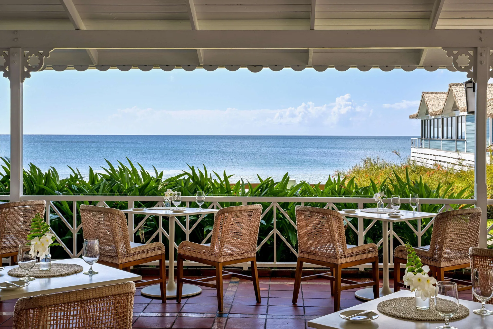 Open-air oceanfront dining tables with wicker chairs at Sandals Halcyon.