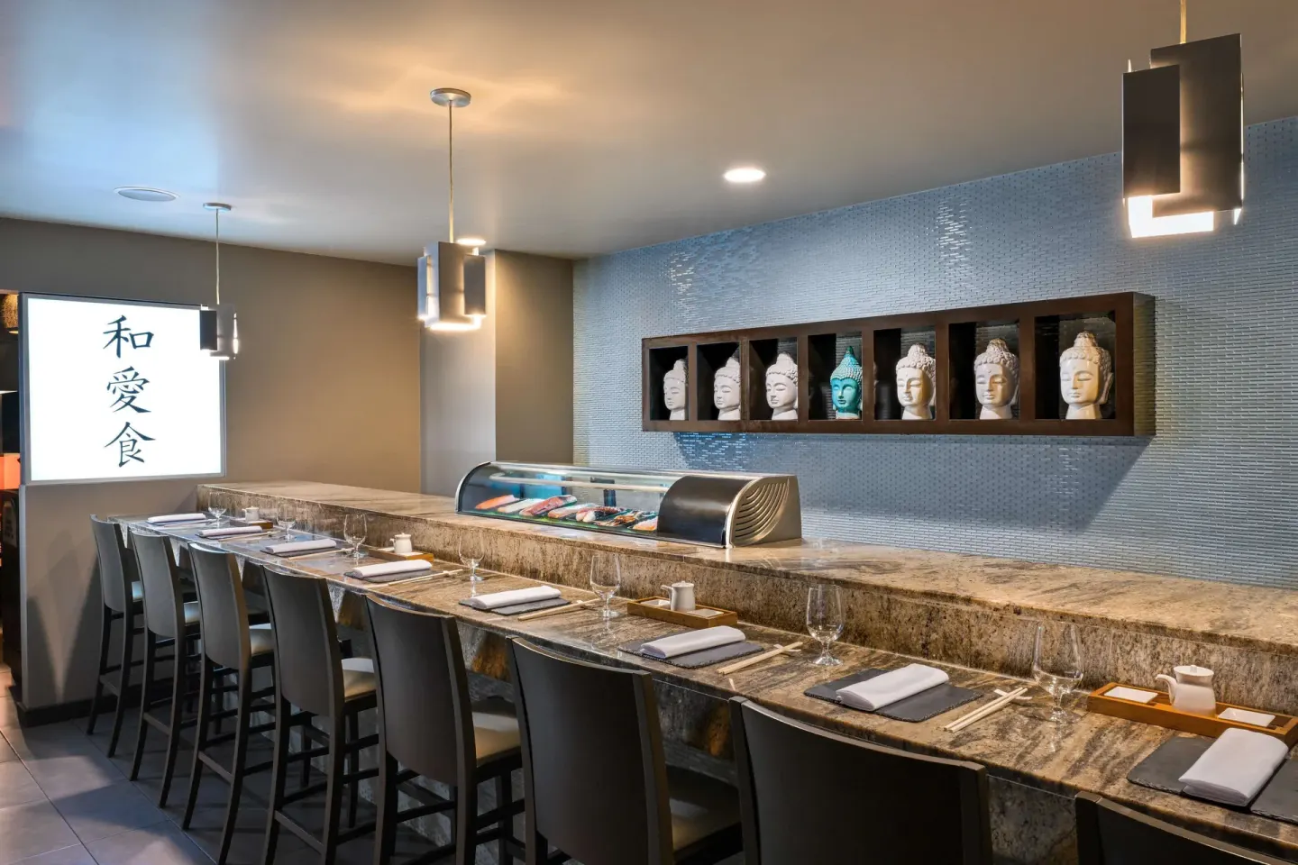 Sushi bar counter with place settings, display case, and decorative busts at Sandals Halcyon.