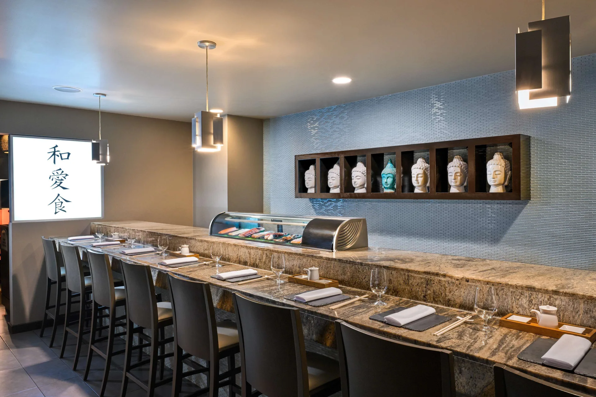 Sushi bar counter with place settings, display case, and decorative busts at Sandals Halcyon.