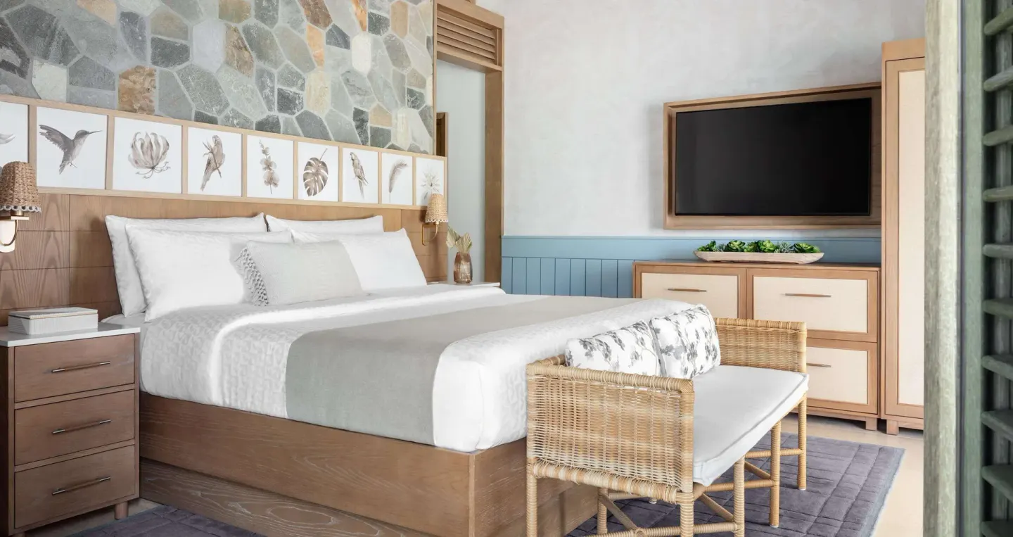 King bed, woven bench, and dresser in a Shore House Butler Suite at Sandals Halcyon.