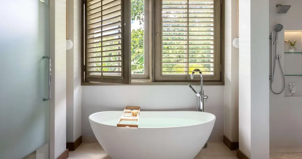Suite bathroom with freestanding tub, shuttered windows and shower at Sandals Halcyon.