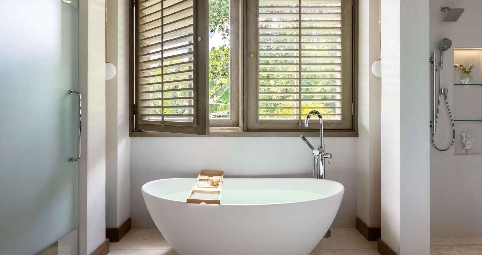 Suite bathroom with freestanding tub, shuttered windows and shower at Sandals Halcyon.