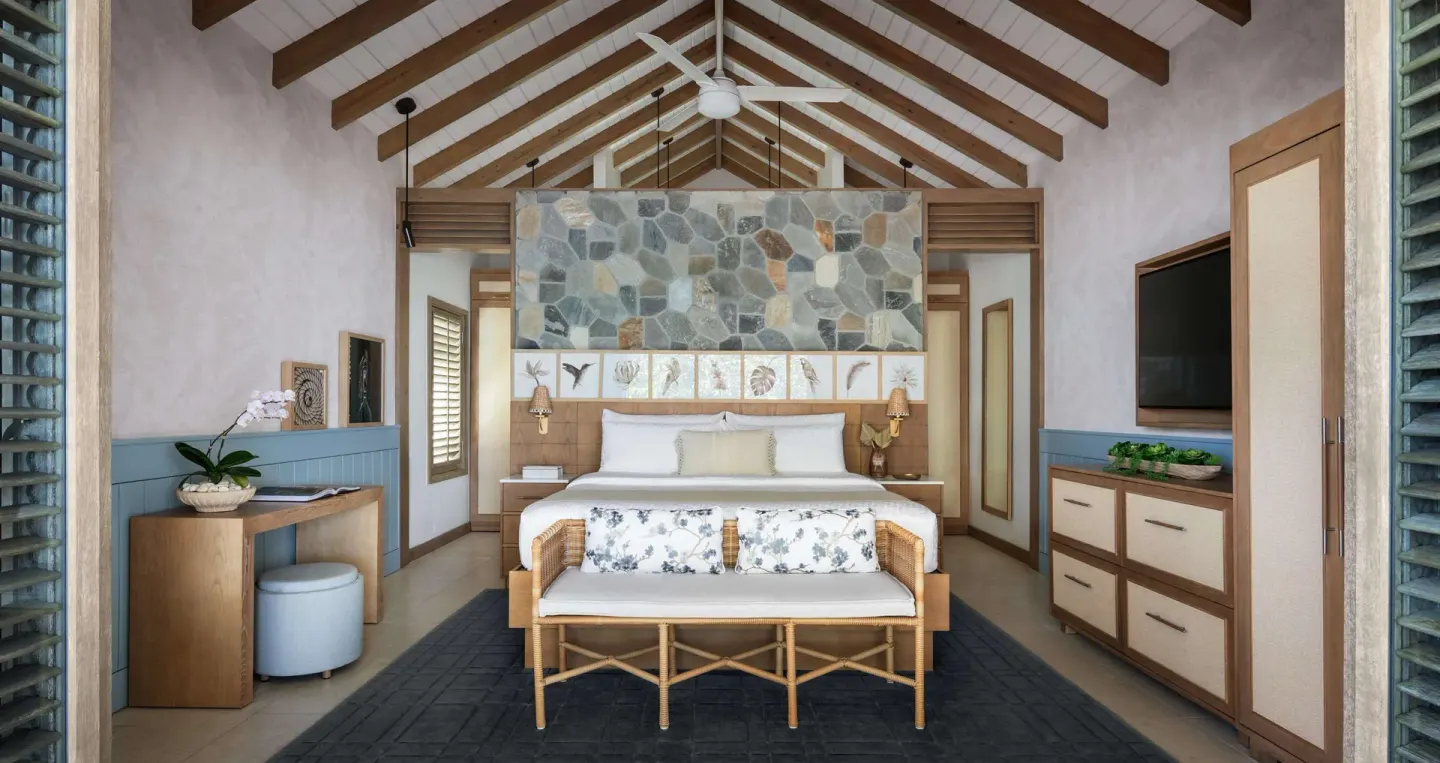 King bed with vaulted ceiling and stone accent wall in a Shore House Butler Suite at Sandals Halcyon.