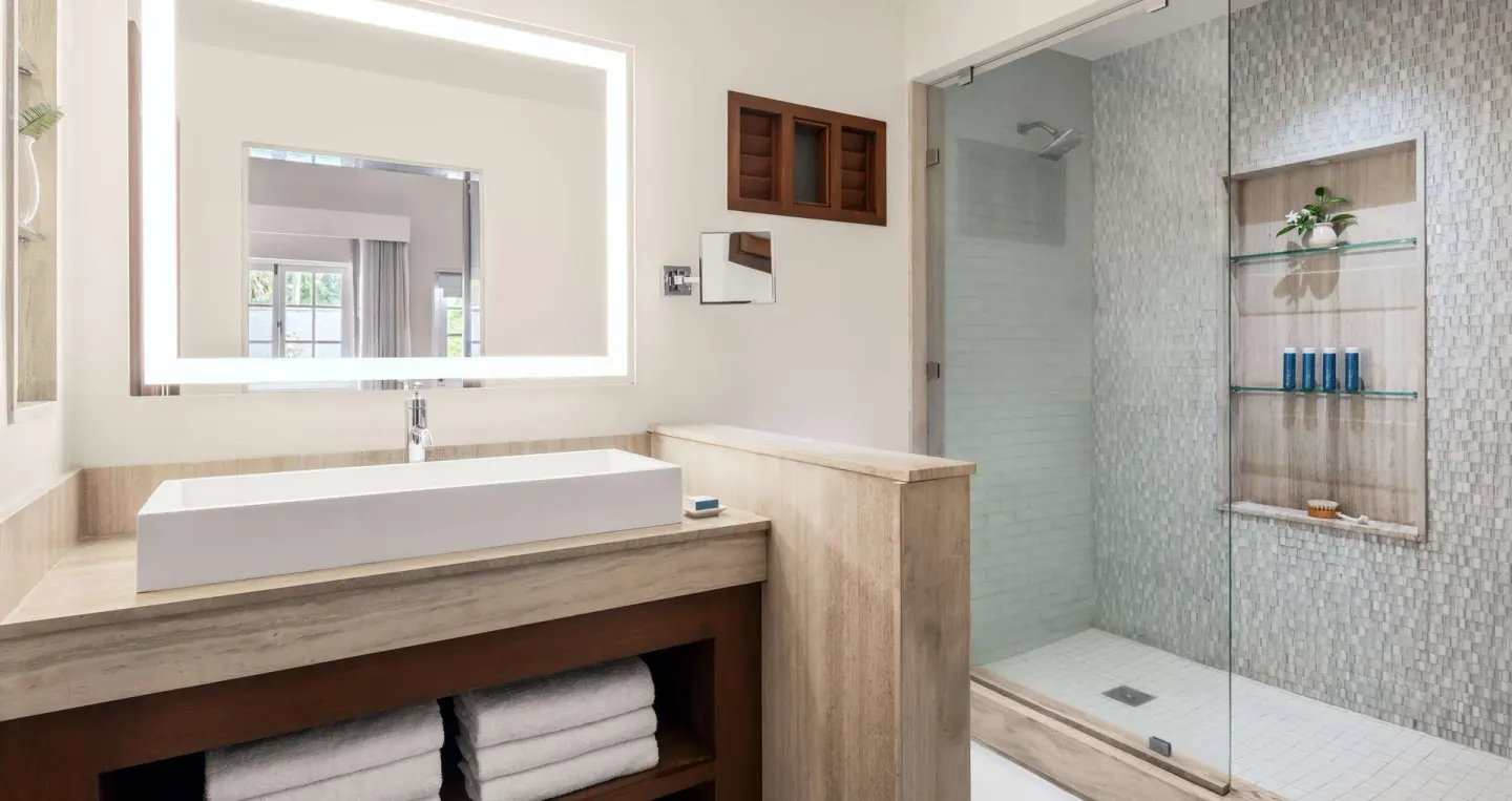 Modern bathroom with illuminated mirror and glass shower at Sandals Halcyon.