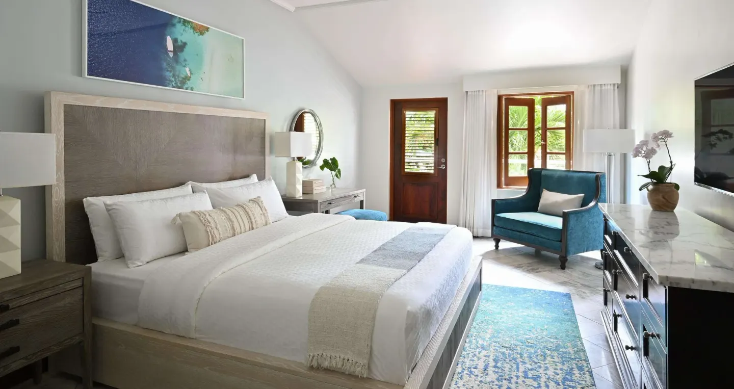 Luxury room king bed with teal chair and dresser at Sandals Halcyon.