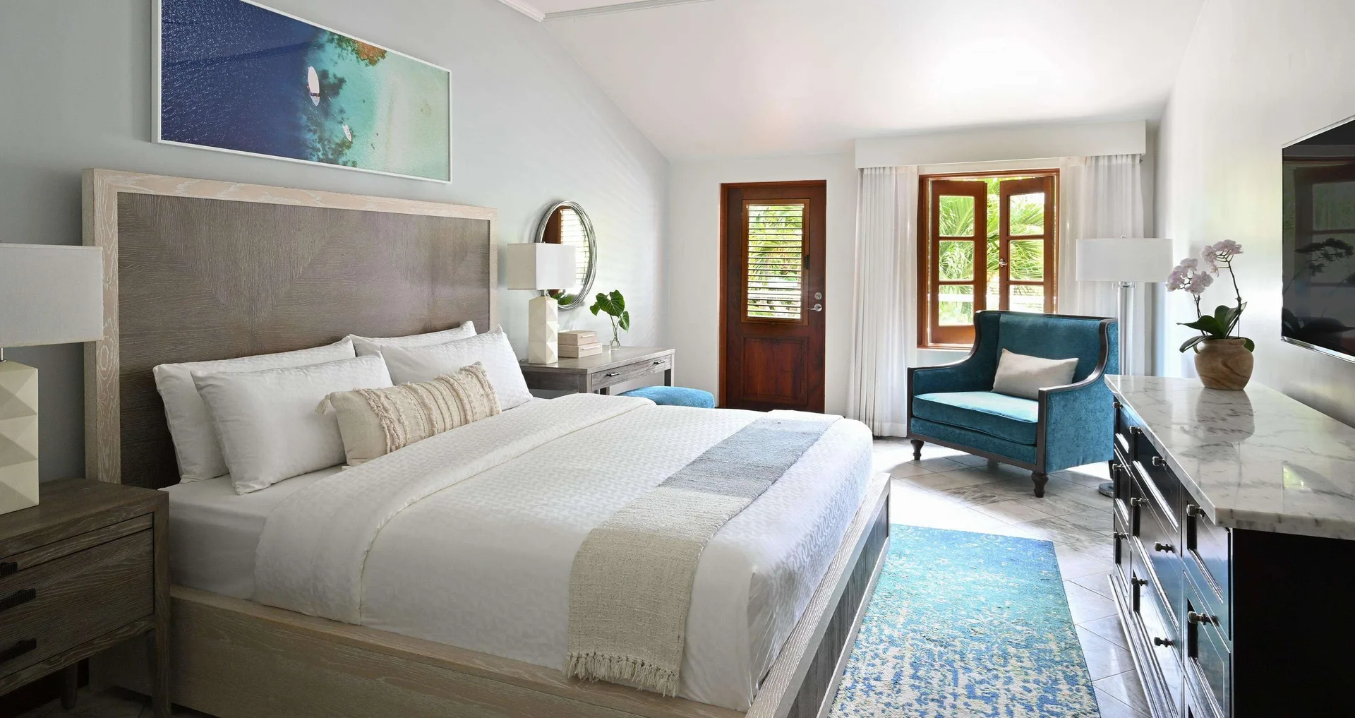 Luxury room king bed with teal chair and dresser at Sandals Halcyon.