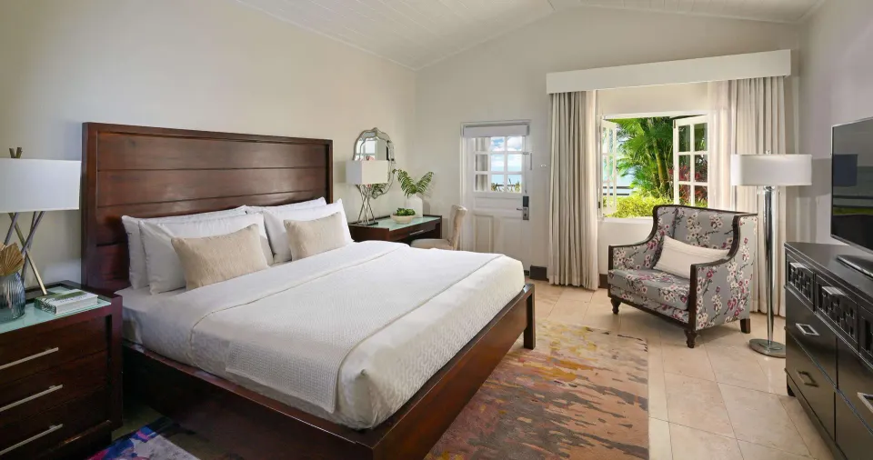 Luxury Room king bed, sitting area and garden-facing window at Sandals Halcyon.