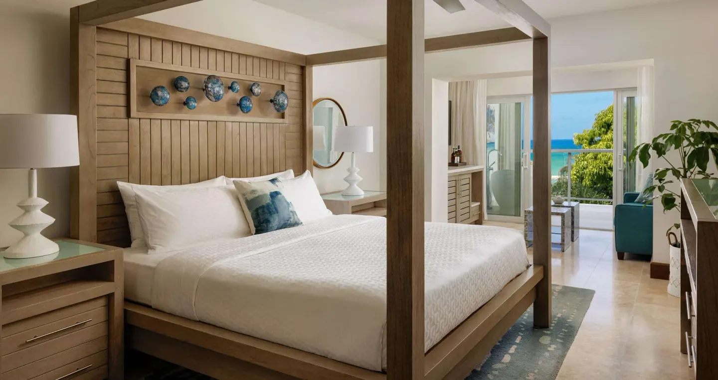 Four-poster king bedroom with balcony and ocean glimpse at Sandals Montego Bay.