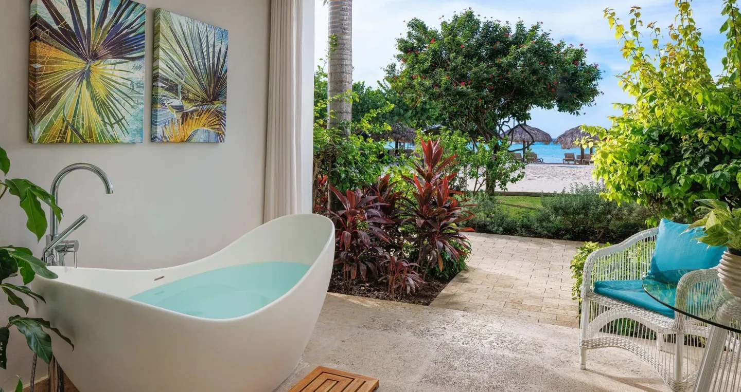 Open-air patio soaking tub with garden plants and beach beyond at Sandals Montego Bay.