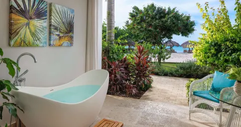 Open-air patio soaking tub with garden plants and beach beyond at Sandals Montego Bay.
