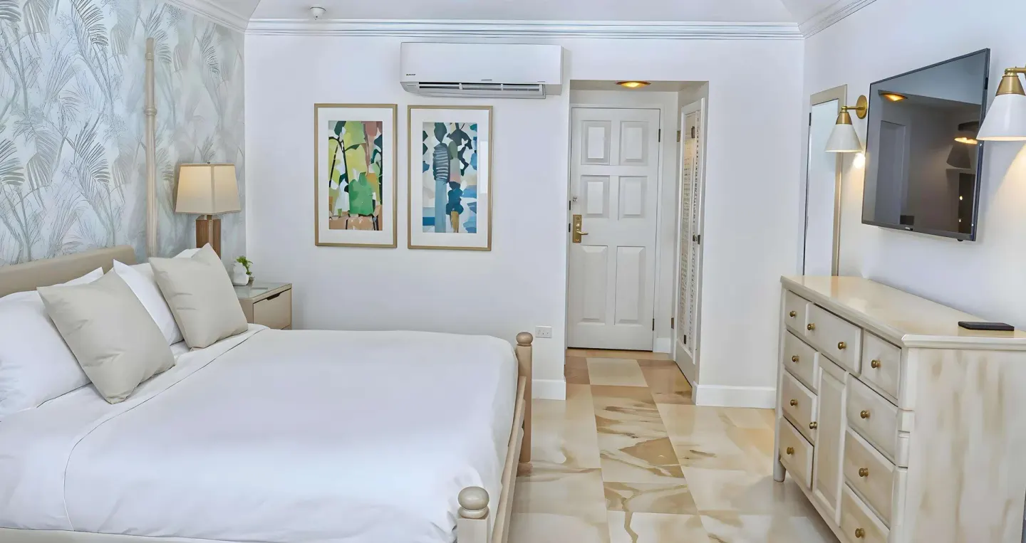 King bed, dresser, wall-mounted TV, and entry door in a guest room at Sandals Montego Bay.