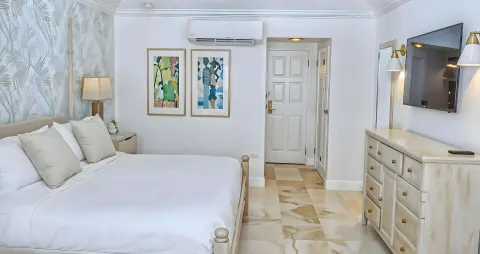 King bed, dresser, wall-mounted TV, and entry door in a guest room at Sandals Montego Bay.
