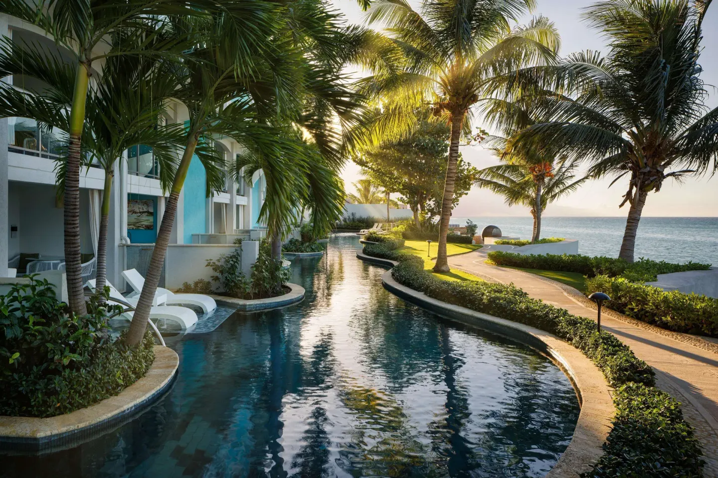 Winding swim-up pool beside palm trees and the ocean at Sandals Montego Bay.