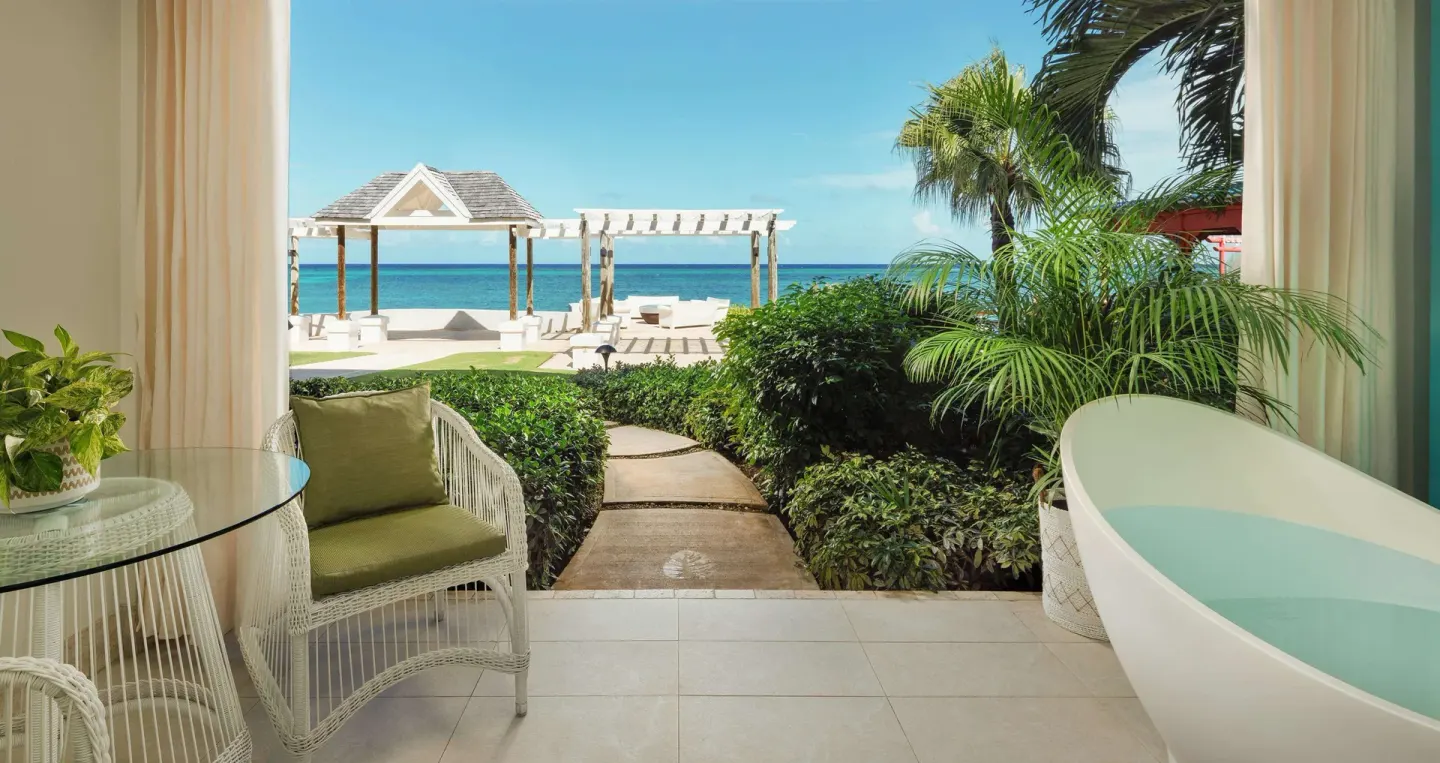Private patio with soaking tub, wicker chair, garden path, and ocean view at Sandals Montego Bay.
