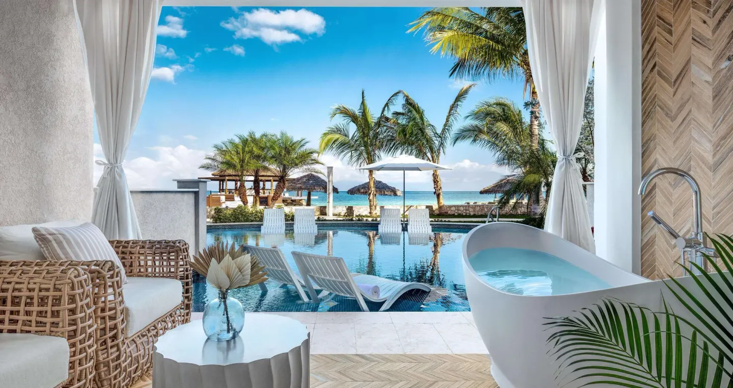 Patio soaking tub beside a pool with palm trees and ocean beyond at Sandals Montego Bay.