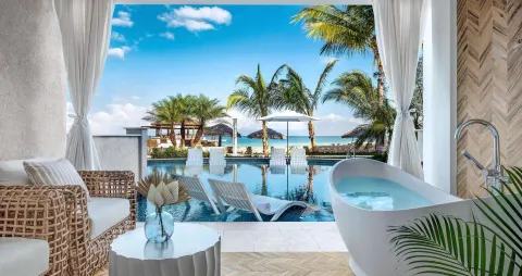 Patio soaking tub beside a pool with palm trees and ocean beyond at Sandals Montego Bay.