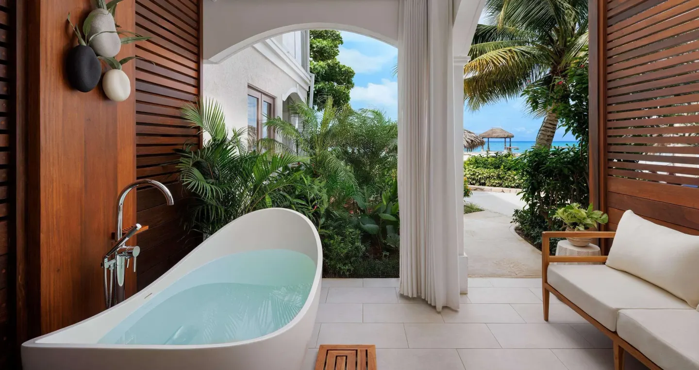 Private patio with soaking tub, wood shutters, sofa, and garden path at Sandals Montego Bay.