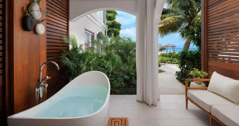 Private patio with soaking tub, wood shutters, sofa, and garden path at Sandals Montego Bay.