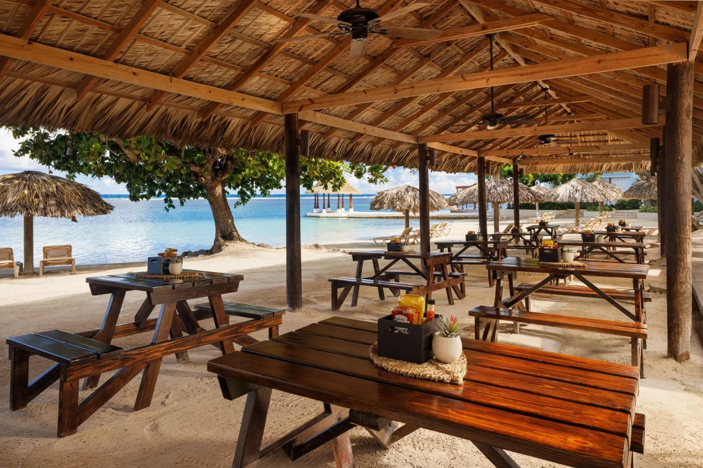 Beachfront open-air picnic tables under a thatched roof at Sandals Montego Bay.