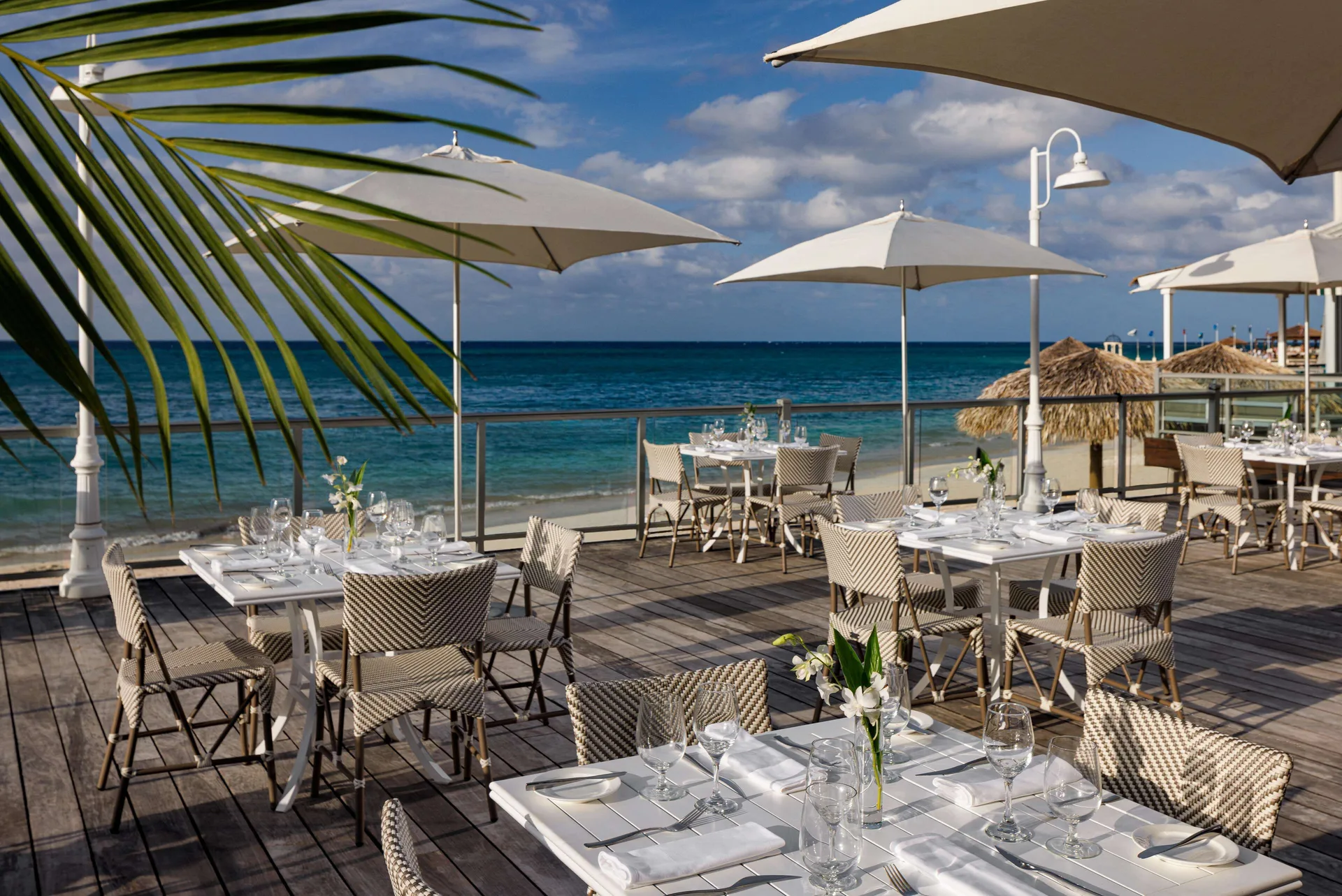 Seaside deck with white umbrellas and set dining tables at Sandals Montego Bay.