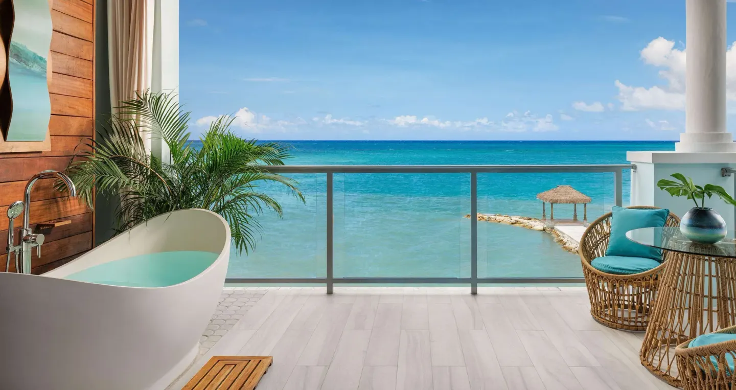 Beachfront balcony at Sandals Montego Bay with soaking tub, wicker seating, and ocean view.