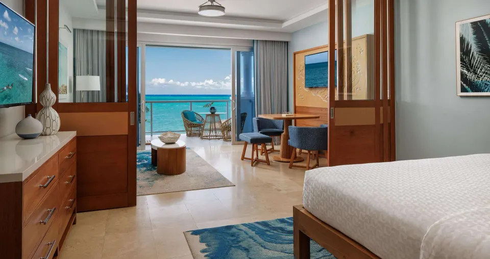 One-bedroom ocean-view suite at Sandals Montego Bay with bed, lounge, dining table, and balcony.
