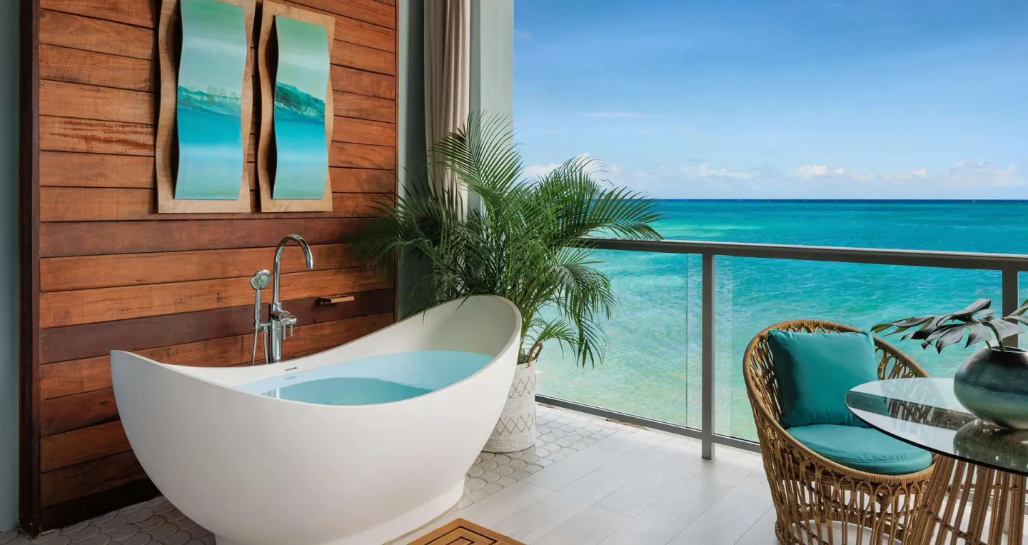 Balcony soaking tub at Sandals Montego Bay beside wicker seating and a wide ocean view.