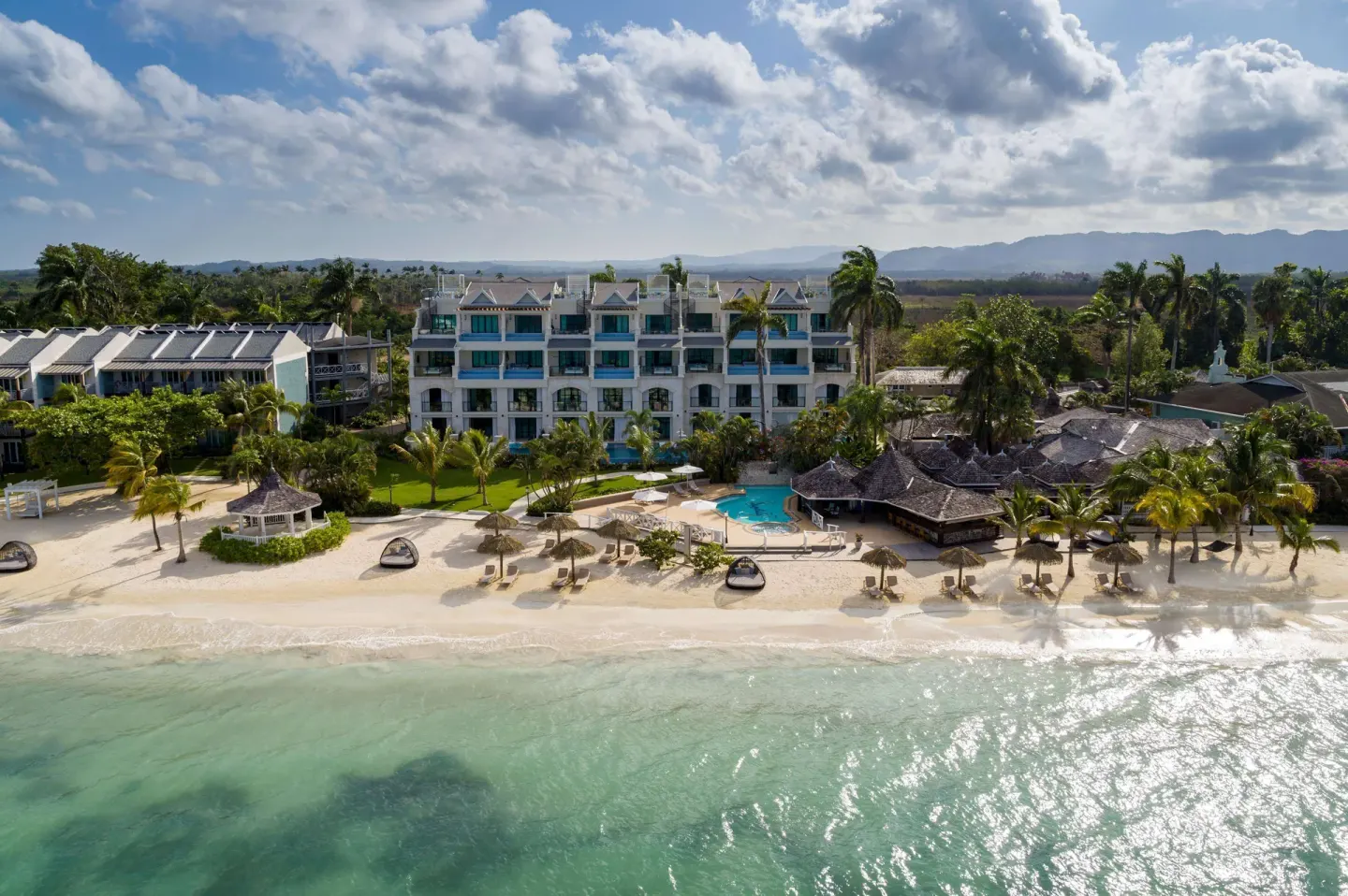 Aerial beachfront view of white resort buildings, palms, pool and sea at Sandals Negril.