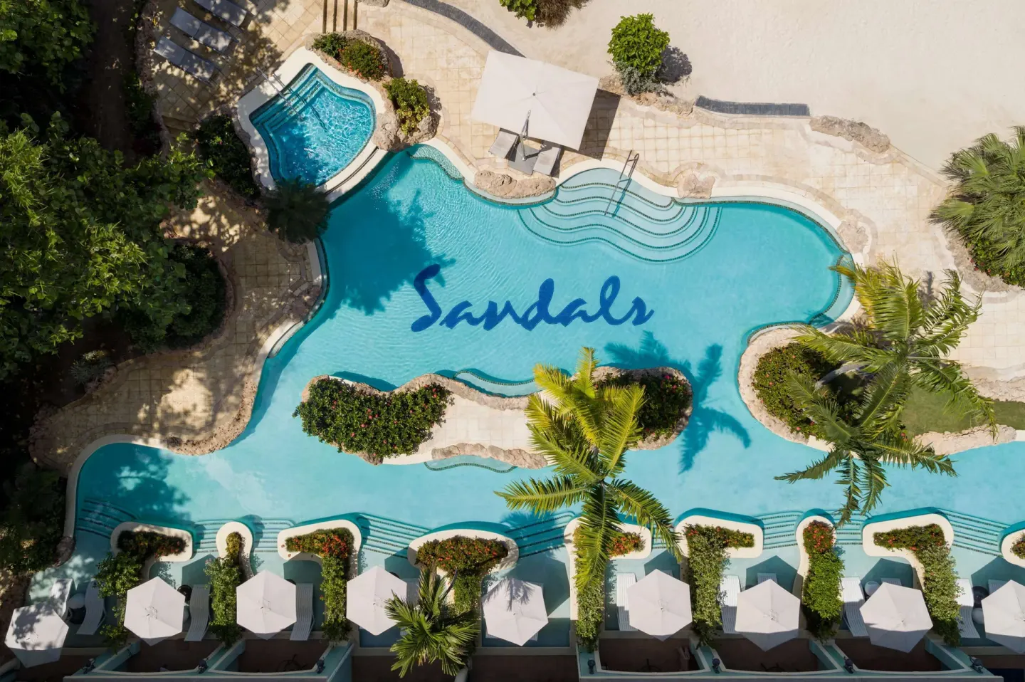 Aerial view of a winding pool with palms, cabanas, and beach sand at Sandals Negril.