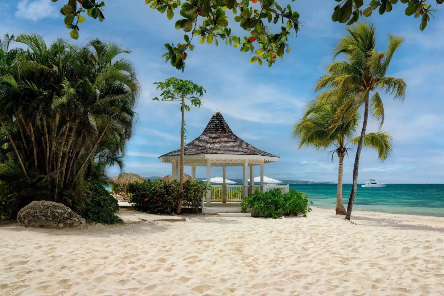 White beach gazebo framed by palms and tropical greenery at Sandals Negril.