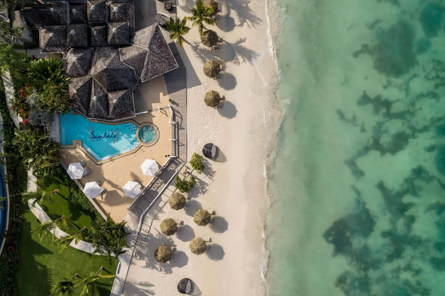 Aerial view of a beachfront pool, sandy beach, and clear water at Sandals Negril.