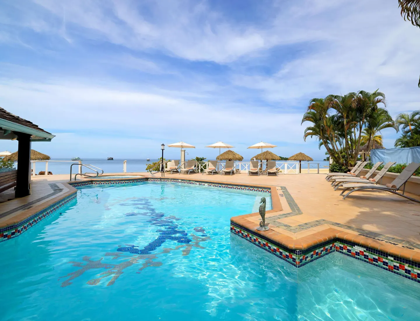 Beachfront pool with loungers, umbrellas, and ocean views at Sandals Negril.