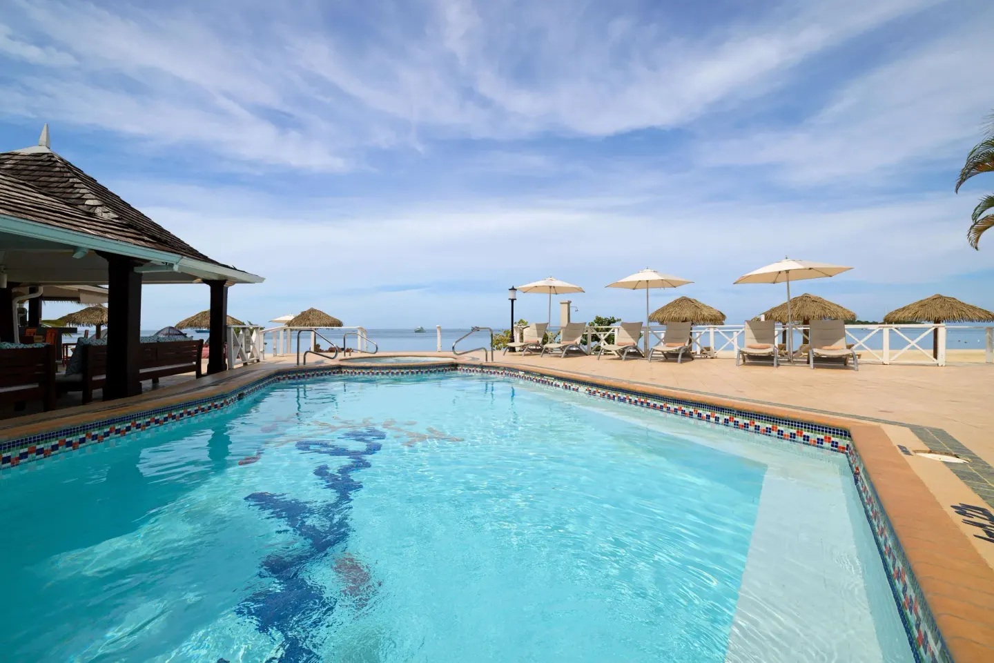 Beachfront pool with umbrellas, loungers, and thatched shade huts at Sandals Negril.