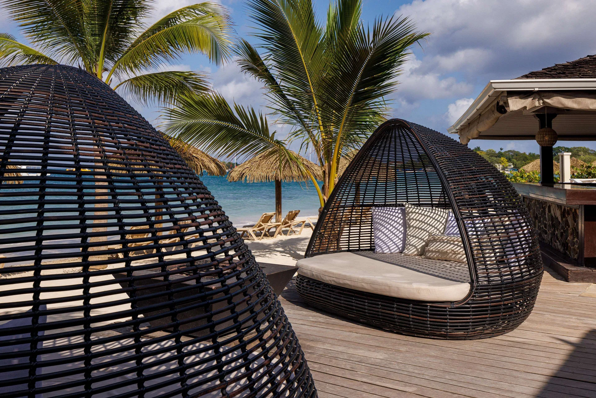 Wicker pod loungers with cushions on a beachfront deck at Sandals Negril.