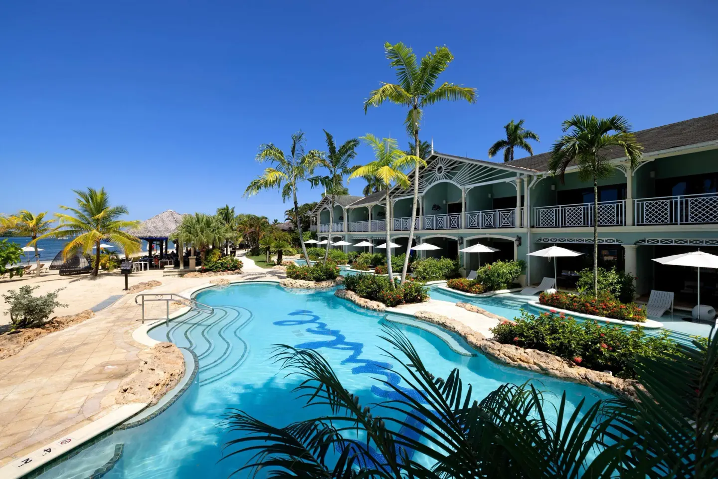 Curved resort pool with palm trees, loungers, and the beach nearby at Sandals Negril.