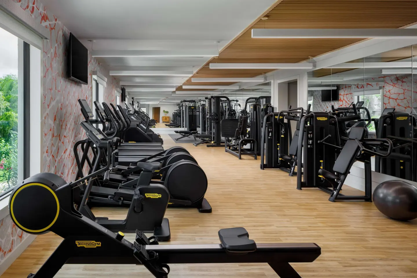 Fitness center with cardio machines, strength equipment, mirrors, and wood flooring at Sandals Negril.