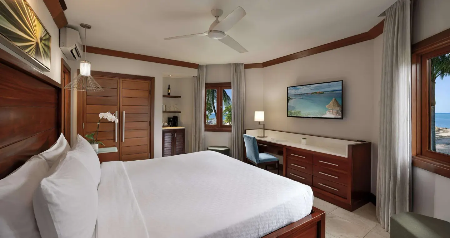 Guest room with a king bed, desk, and windows looking toward the beach at Sandals Negril.