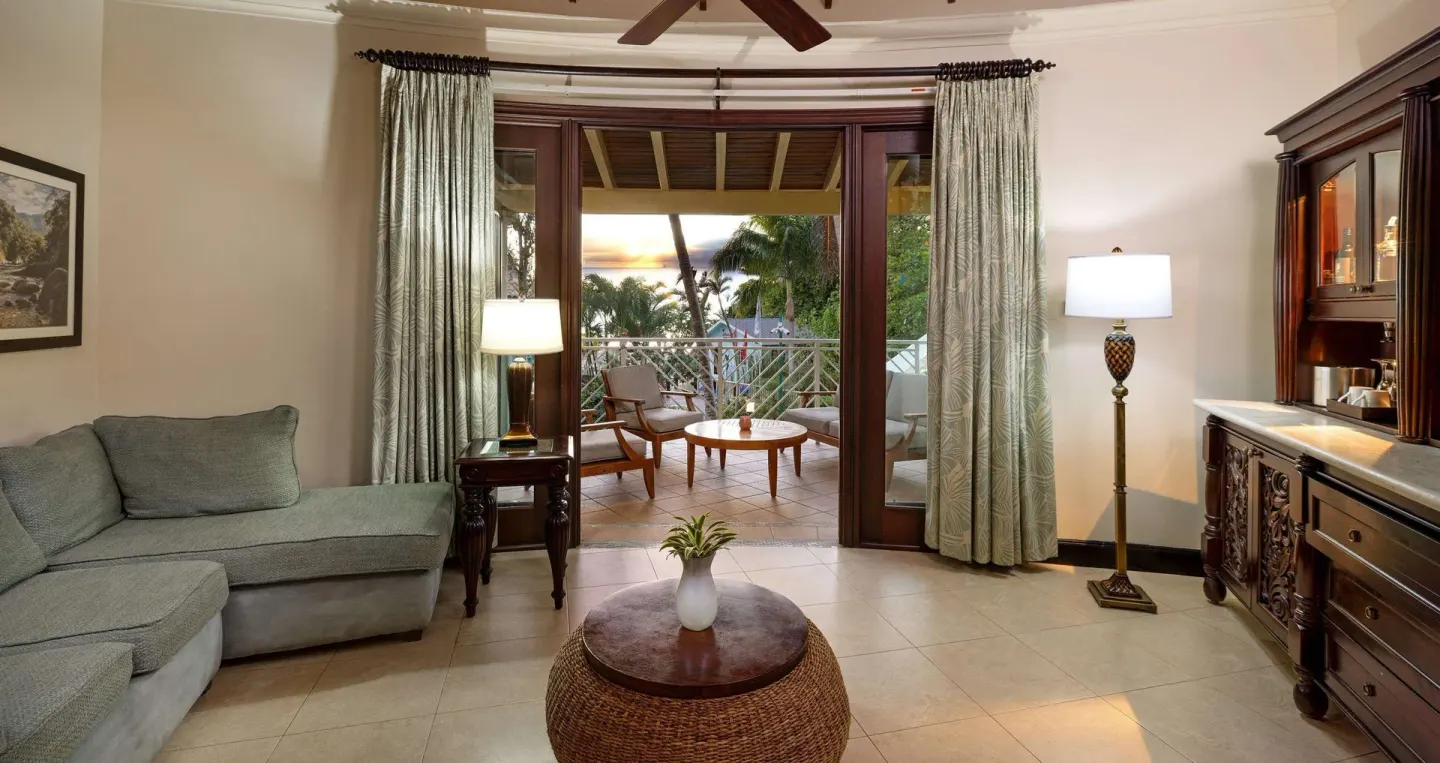 Living area with sofa, wet bar, and balcony facing sunset views at Sandals Negril.