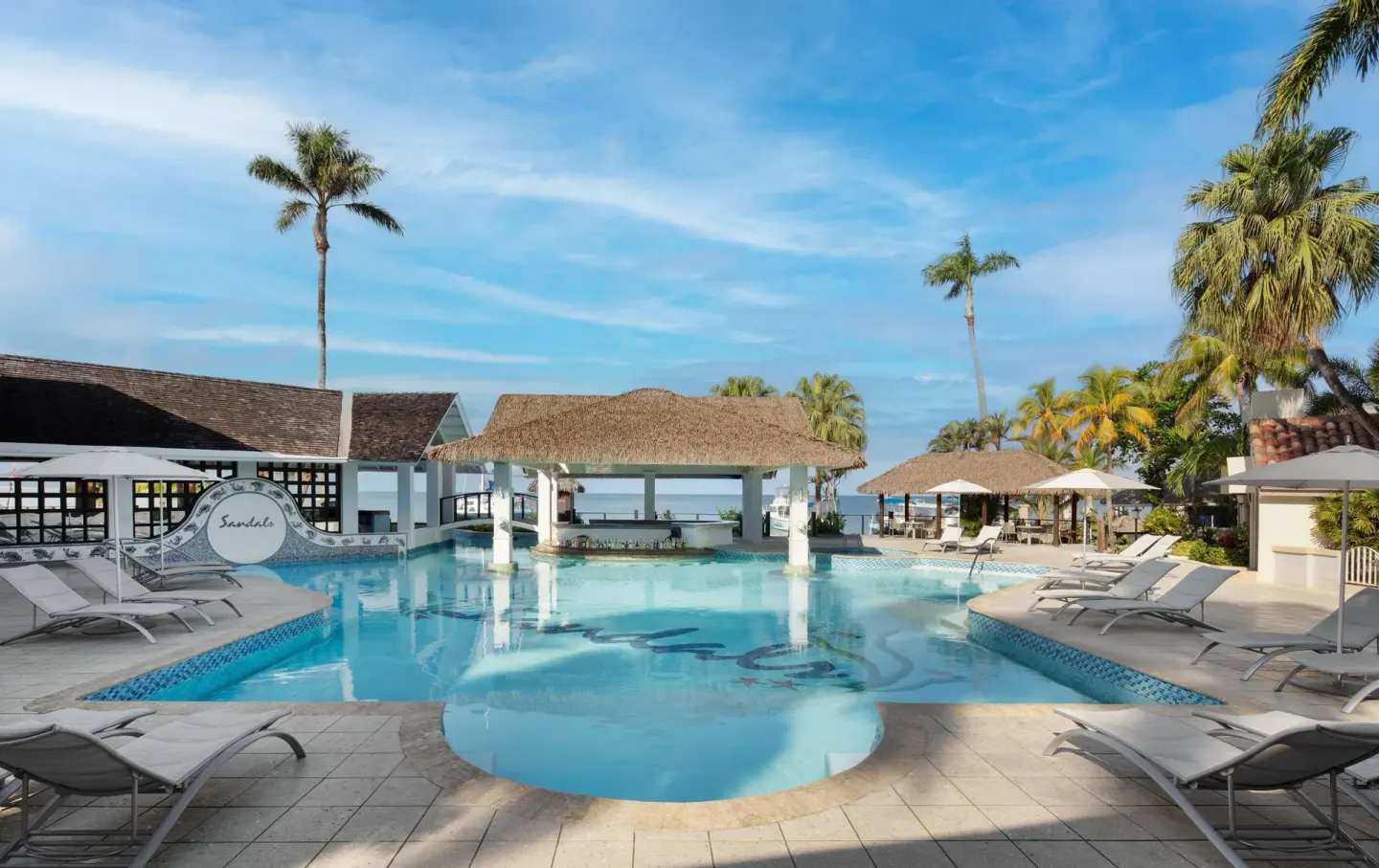 Large pool with a thatched swim-up bar, loungers, palms, and sea beyond at Sandals Negril.