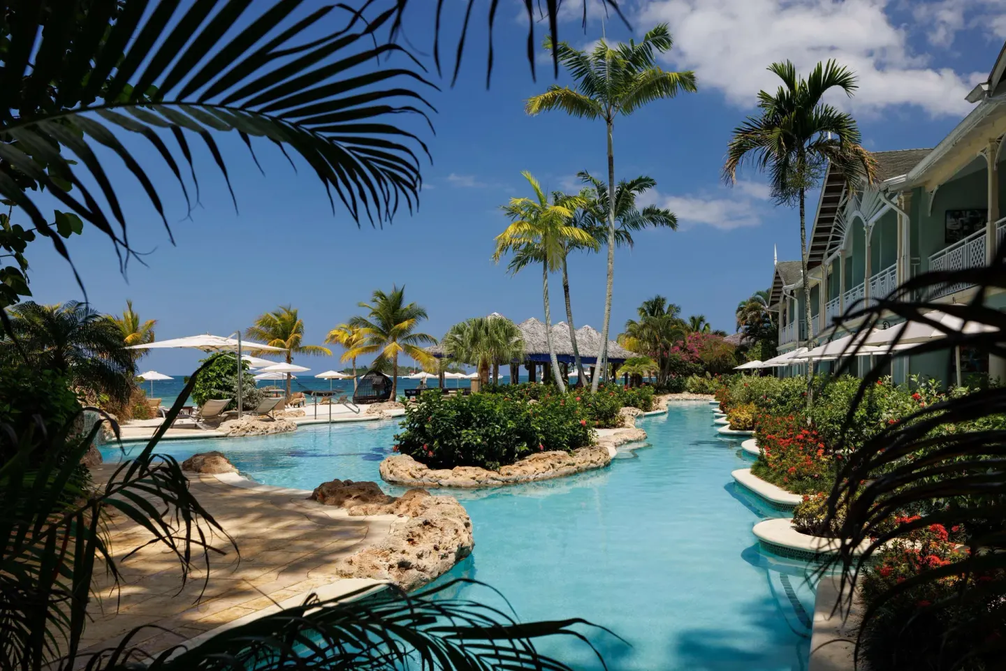 Tropical pool framed by palm fronds with the ocean beyond at Sandals Negril.