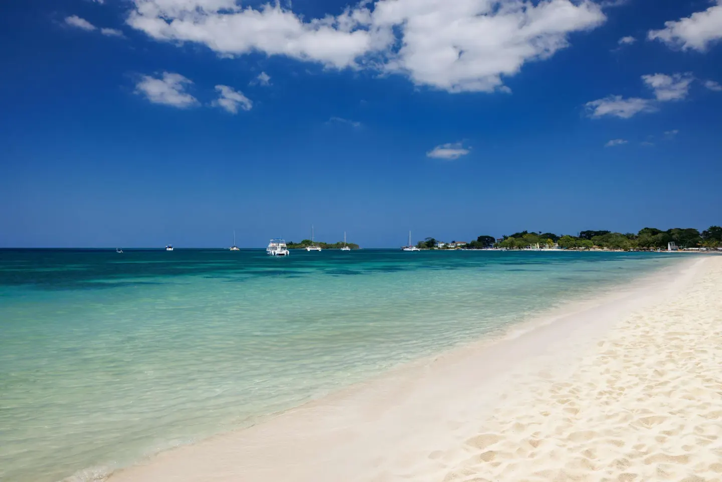 White sand beach and calm turquoise water with boats at Sandals Negril.