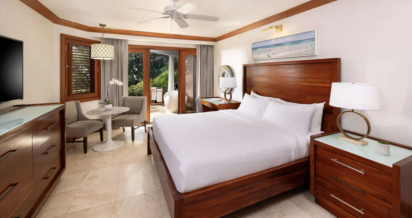King bed guest room with seating area and balcony doors at Sandals Negril.