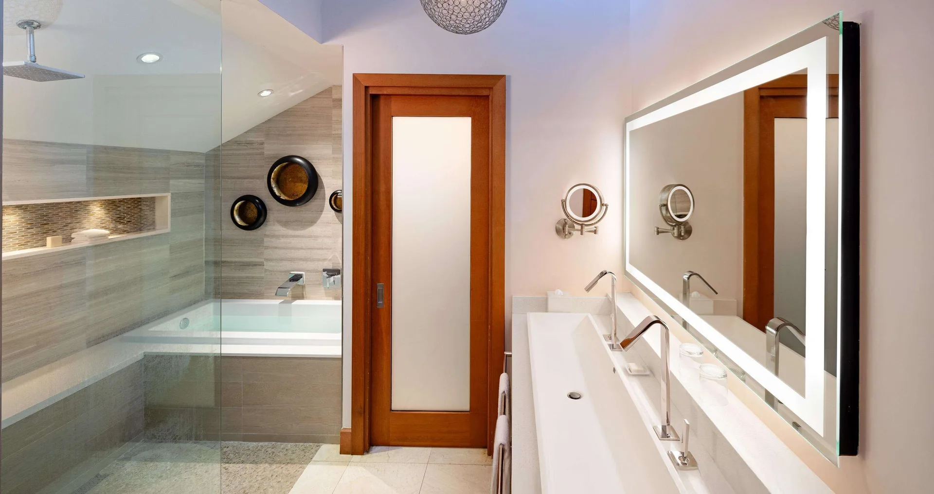Bathroom in a villa suite at Sandals Negril with double vanity, lit mirror, shower and tub.